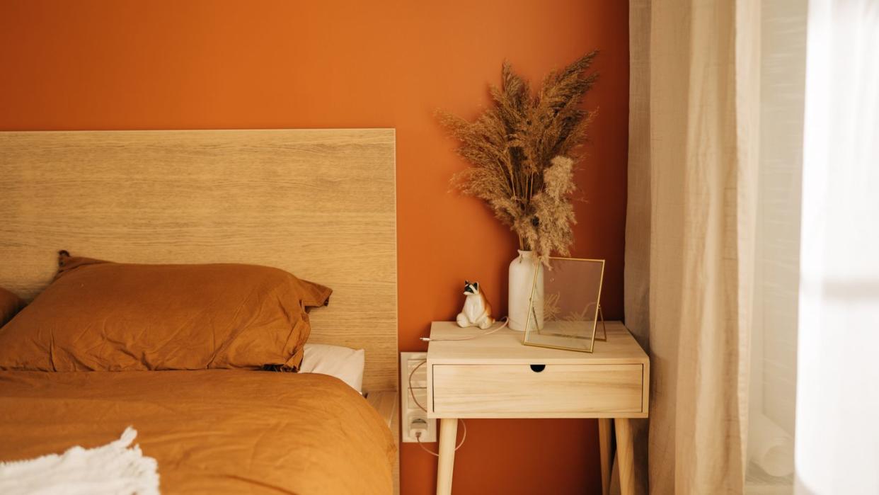 close up on simple, white bedside table with decorations next to comfortable bed in bedroom with dark blue wall