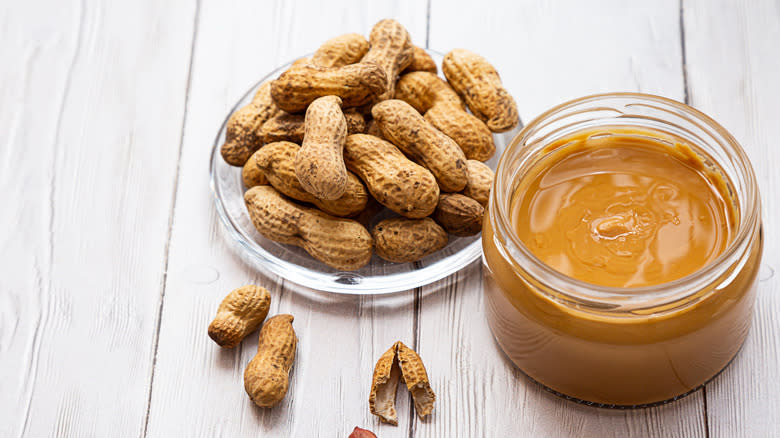 A jar of peanut butter beside peanuts