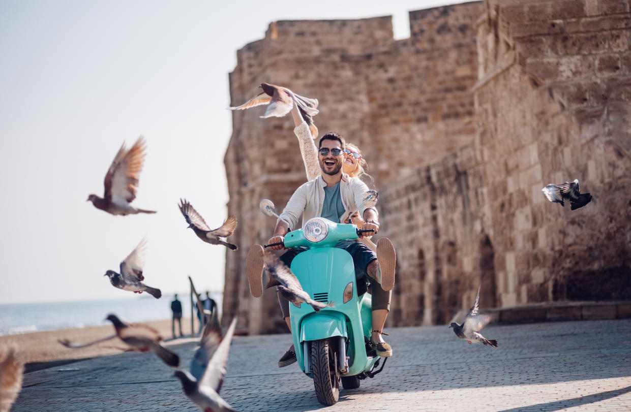 Tourist on summer holidays in Europe having fun riding retro scooter by the sea as part of weekly travel deals with yahoo lifestyle