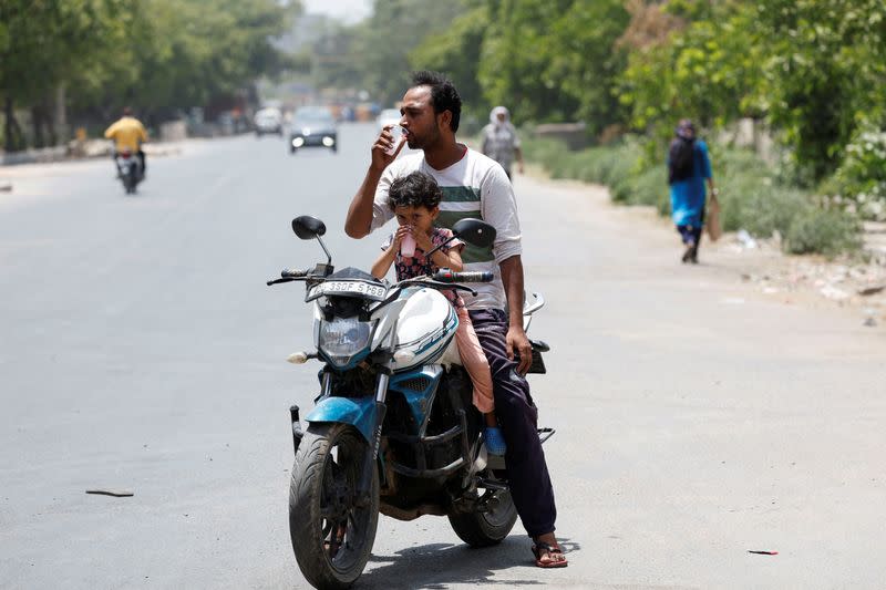A man and a child drink cooling drinks offered by locals on a hot summer day in Narela