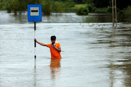 A man holds a bus stop post on a flooded road as he waits for a military vehicle to go to a town, in Bulathsinhala village, in Kalutara, Sri Lanka May 27, 2017. REUTERS/Dinuka Liyanawatte