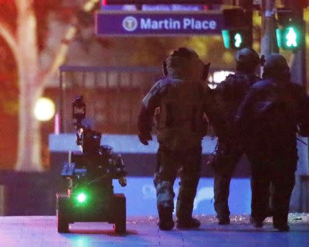 Police officers wearing armoured suits walk with a robot towards Lindt Cafe in Martin Place in central Sydney December 16, 2014. REUTERS/Jason Reed