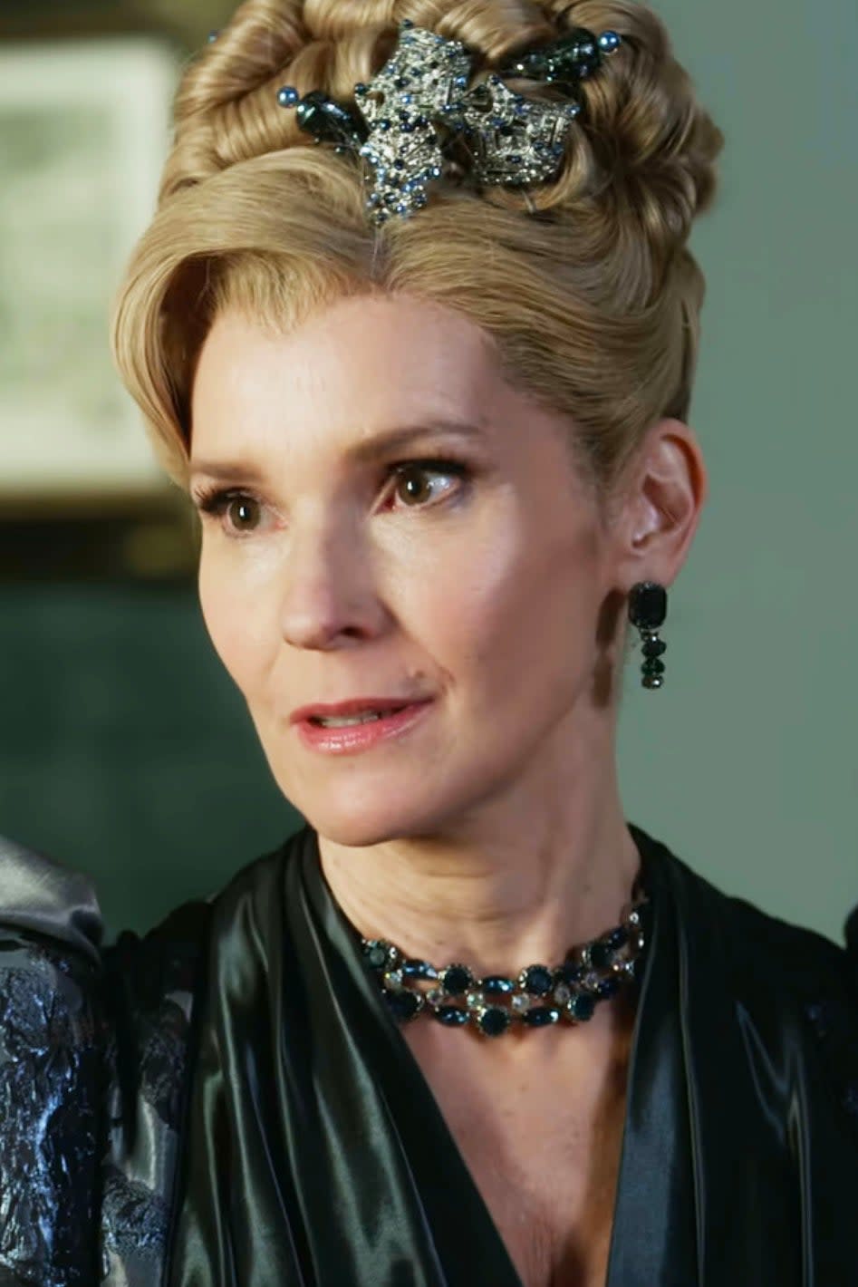 Joanna Bobin as Lady Araminta Cowper with an intricate updo hairstyle, wearing a detailed period gown and jewelry, in a scene with candelabra in the background