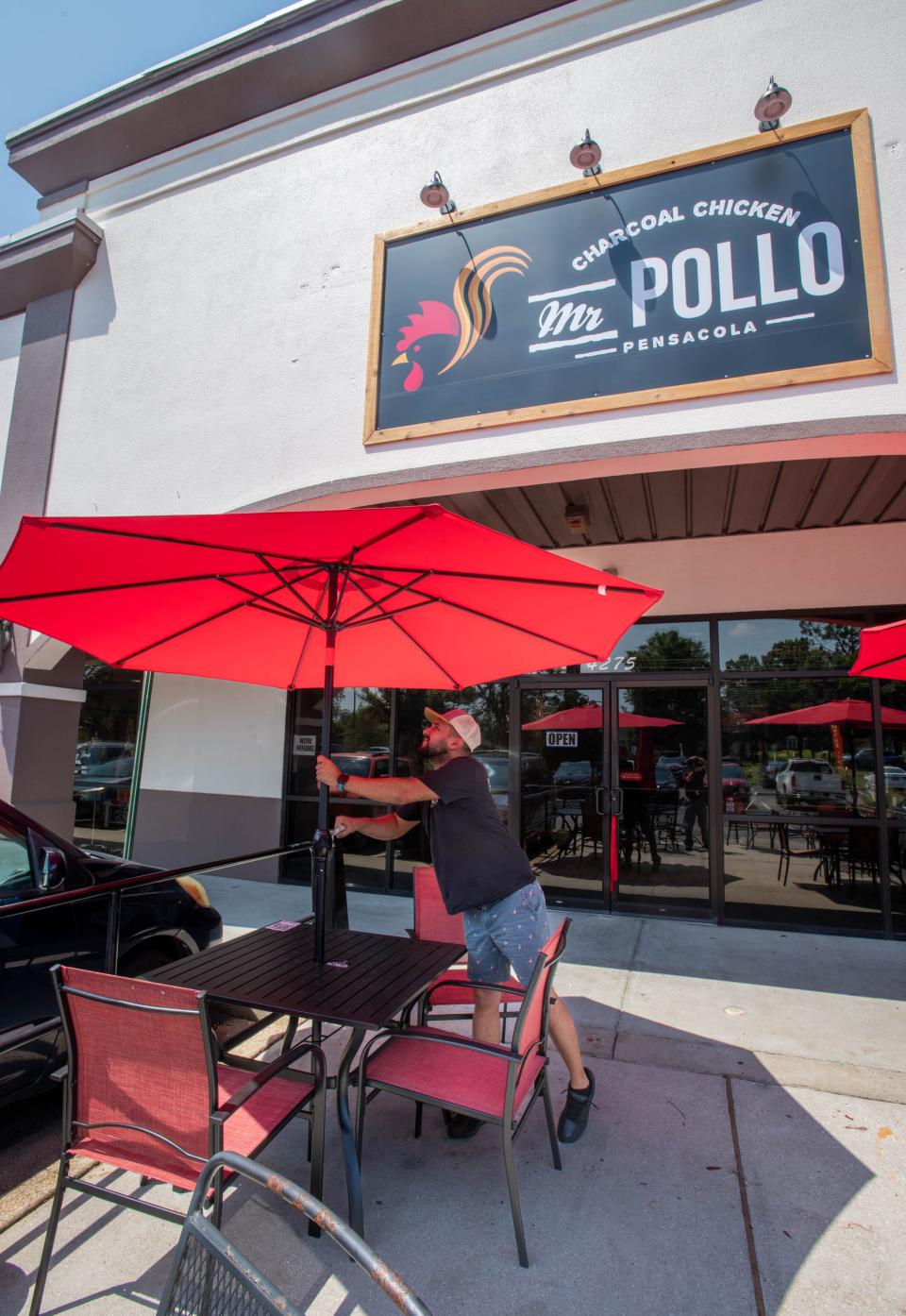 Oscar Paredes raises umbrellas for outdoor seating at the new second location of Mr. Pollo on Woodbine Road in Pace on Friday, June 30, 2023.