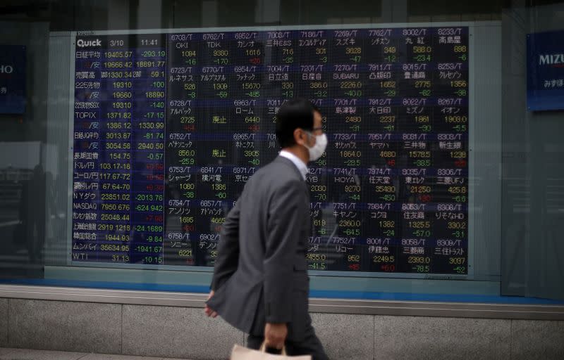 FILE PHOTO: A man wearing protective face mask walks in front of a stock quotation board outside a brokerage in Tokyo