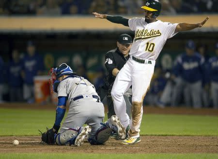 Aug 8, 2018; Oakland, CA, USA; Oakland Athletics shortstop Marcus Semien (10) signals safe after sliding home ahead of the relay to Los Angeles Dodgers catcher Yasmani Grandal (left) during the eighth inning at Oakland Coliseum. Making the official call is umpire is Mike Muchlinski (middle). D. Ross Cameron-USA TODAY Sports