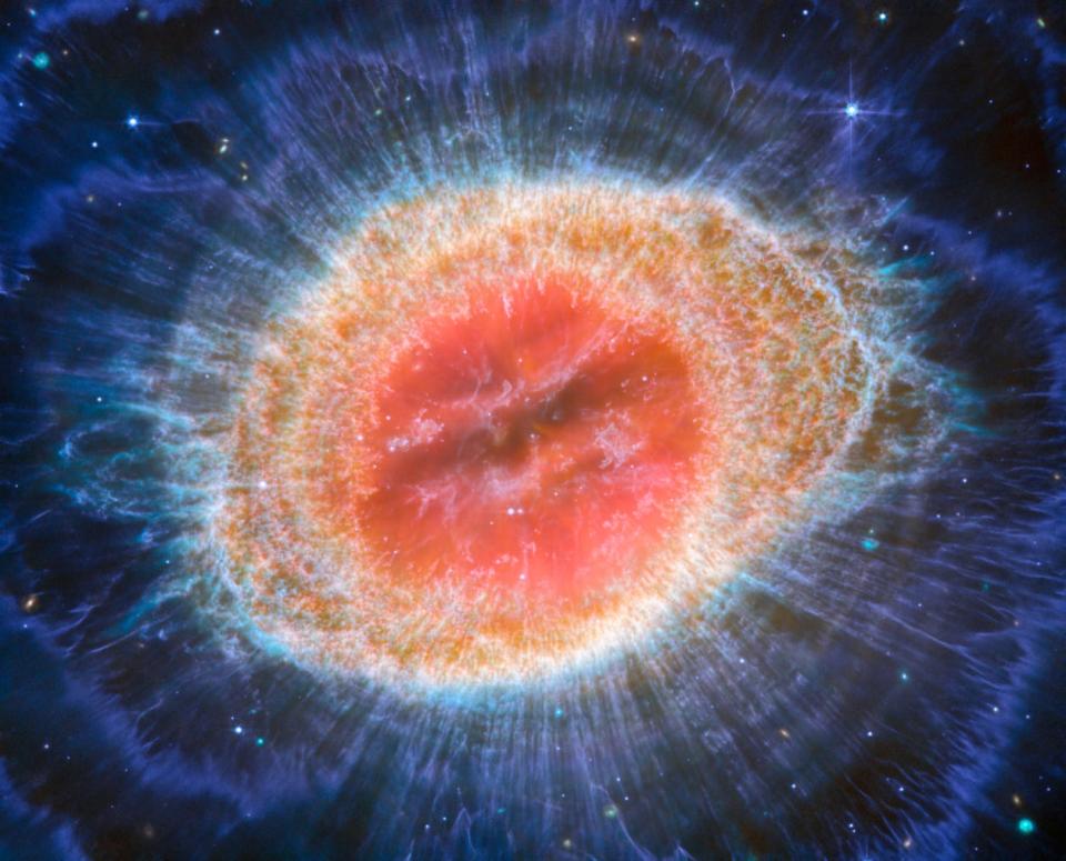 nebula in space with a pink bubble center and a textured orange ring surrounding it with wavy blue hazy lines and faint concentric arcs expanding out into space