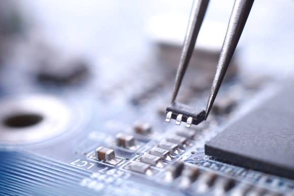 Technician using tweezers to install a microchip on a circuit board.