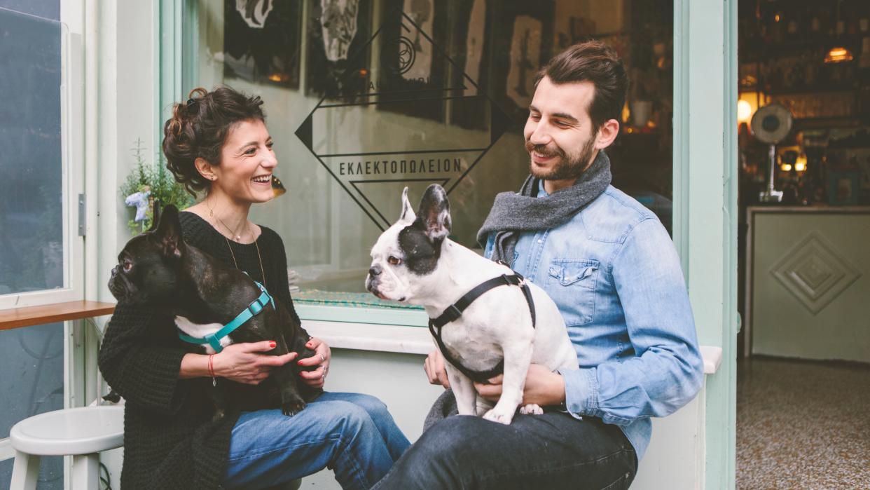  Couple sat outside cafe with dogs on their laps. 