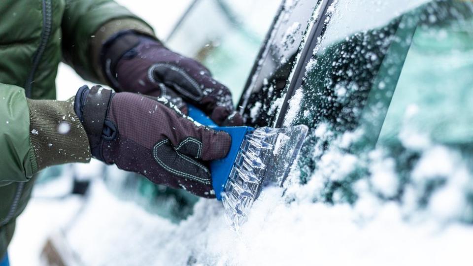 A man wearing gloves while de-icing his car