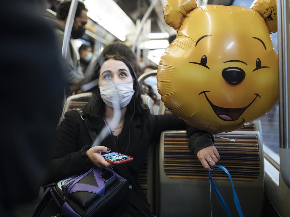 A masked woman holds a Winnie the Pooh inflatable balloon, inside the subway, in Paris, Thursday Oct.29, 2020. Some doctors expressed relief but business owners despaired as France prepared to shut down again for a month to try to put the brakes on the fast-moving virus. (AP Photo/Lewis Joly)