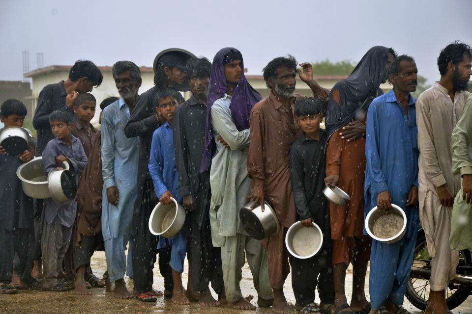 People wait in the rain for their turn to receive free food distributed by volunteers outside a camp of internally displaced people from coastal areas in Sujawal, Pakistan's southern district in the Sindh province, Thursday, June 15, 2023, as Cyclone Biparjoy was approaching. A vast swath of western India and neighboring southern Pakistan that suffered deadly floods last year are bracing for a new deluge as fast-approaching Cyclone Biparjoy whirls toward landfall Thursday. (AP Photo/Pervez Masih)