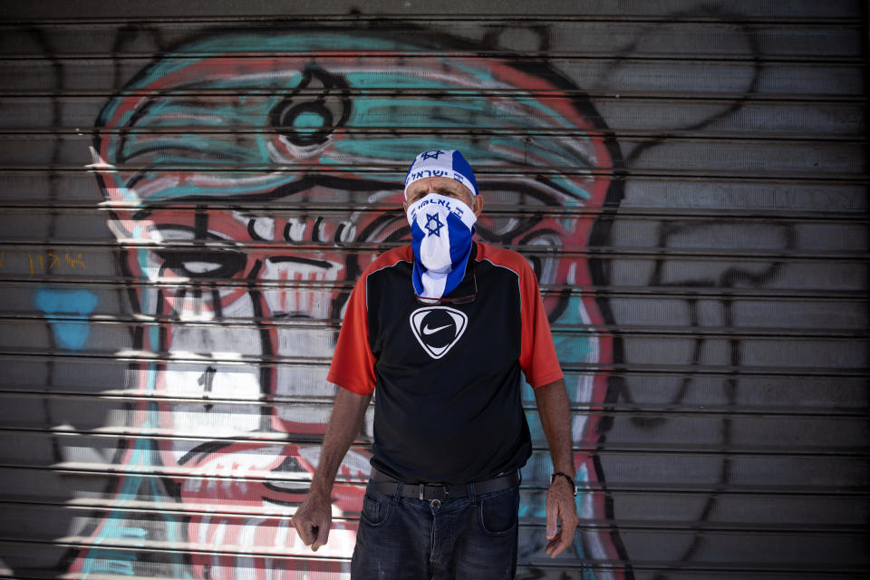A toy store employe wears an improvised protective face mask in the colors of the national flag amid concerns over the country's coronavirus outbreak, calls for clients outside the store, in Tel Aviv, Israel, Tuesday, April 28, 2020. Israel's government announced a complete lockdown over the upcoming Israel's 72nd Independence Day to control the country's coronavirus outbreak. (AP Photo/Oded Balilty)