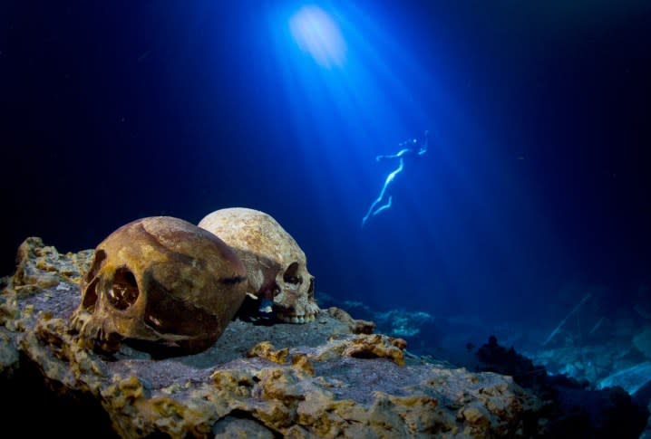 Mayan skulls in a sand with a swimmer behind it.