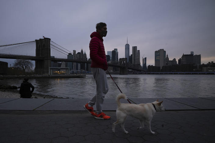 A man wearing a mask walks his dog in Brooklyn Bridge Park on Tuesday during the coronavirus pandemic in New York.