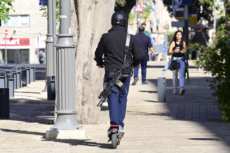 A man carrying an assault rifle rides an electric scooter down a sidewalk in central Jerusalem on December 8, 2023.