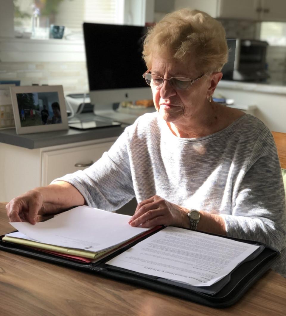 Claire Auger is seen here at her dining room table, looking through a written history of St. Thomas School in Sanford, Maine, on Friday, Oct. 7, 2022. Auger has been a volunteer at the school since it opened 50 years ago.