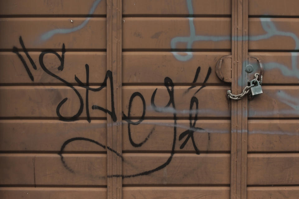 A padlock and chain provides an extra layer of protection on an already locked garage door reportedly tagged by gang members, in Santa Ana, El Salvador, Saturday, Aug. 22, 2020. After years of waiting in countries marred by violence, Central Americans who were approved to come to the U.S. through a small refugee program are facing a major obstacle: the new coronavirus pandemic. (AP Photo/Salvador Melendez)