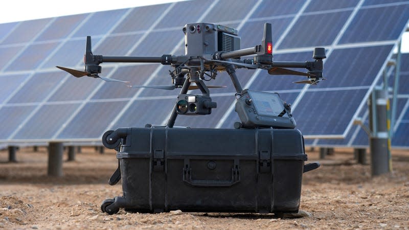 The DJI Matrice 350 RTK powered off an sitting on top of its rolling carrying case, next to a large solar array.