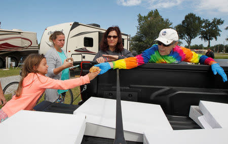 Jordan Taylor (L) reaches for a muffin from Thomas Lowe (R) with Quik Trip who was giving out baked goods along with Sherri Shafranski (L-center) and Michelle Hession at Atlanta Motor Speedway where they were riding out Hurricane Irma in their trailer arriving from Hollywood, Florida in Hampton, Georgia, U.S., September 10, 2017. REUTERS/Tami Chappell