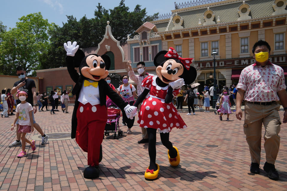 Staff wearing a face mask leads the iconic characters Mickey and Minnie Mouse at the Hong Kong Disneyland, Thursday, April 21, 2022. Hong Kong Disneyland reopened to the public after shutting down due to a surge in COVID-19 infections. (AP Photo/Kin Cheung)