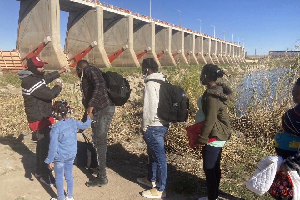 FILE - A Mexican smuggler guides a Haitian family across the Morelos Dam over the Colorado River from Los Algodones, Mexico, on Feb. 4, 2022, to Yuma, Ariz., on the other side. The Biden administration released a plan Tuesday to deal with an increase in already historic numbers of migrants at the U.S.-Mexico border with the lifting of a public health order that has kept people from seeking asylum — and that Republican and some Democratic lawmakers say should be kept in place. (AP Photo/Elliot Spagat, File)