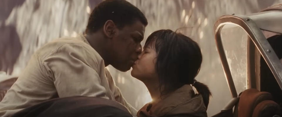 John Boyega and Kelly Marie Tran share a kiss while sitting in a vehicle, with an intense background, in a scene from a movie