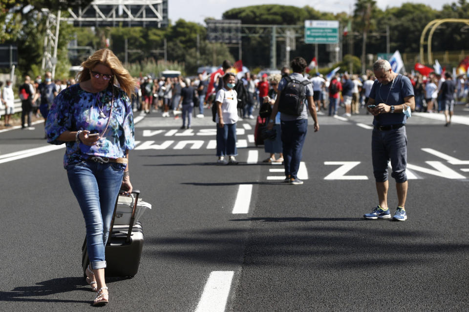 Passengers push their trolleys as Alitalia workers blocked the road leading to the Rome Leonardo Da Vinci international airport following a protest in Fiumicino, Friday, Sept. 24, 2021. Alitalia, which has been in the red for more than a decade, is due to formally exit the airline market next month and be replaced by a new national carrier ITA, or Italy Air Transport. The European Commission has given the go-ahead to a 1.35 billion euro ($1.58 billion) injection of government funding into the new airline, but ITA is only planning to hire around a quarter of the estimated 10,000 Alitalia employees. (Cecilia Fabiano/LaPresse via AP)