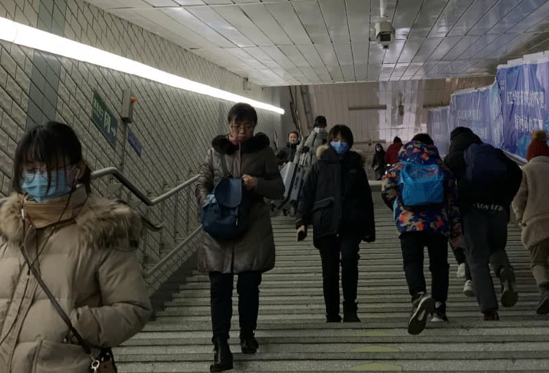 People wearing masks walk down the steps at a subway station in Beijing