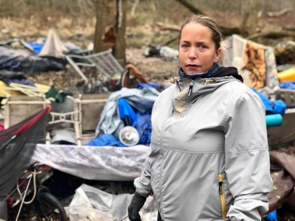 Amy Holman stands in front of a massive pile of debris on the Thames River near the corner of Adelaide and Trafalgar streets. (Rebecca Zandbergen/CBC News - image credit)