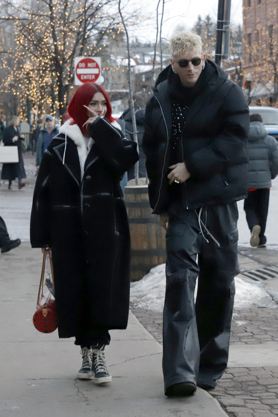 Megan in a long coat with a trim walking on the street with MGK who's wearing a puffy jacket and sunglasses