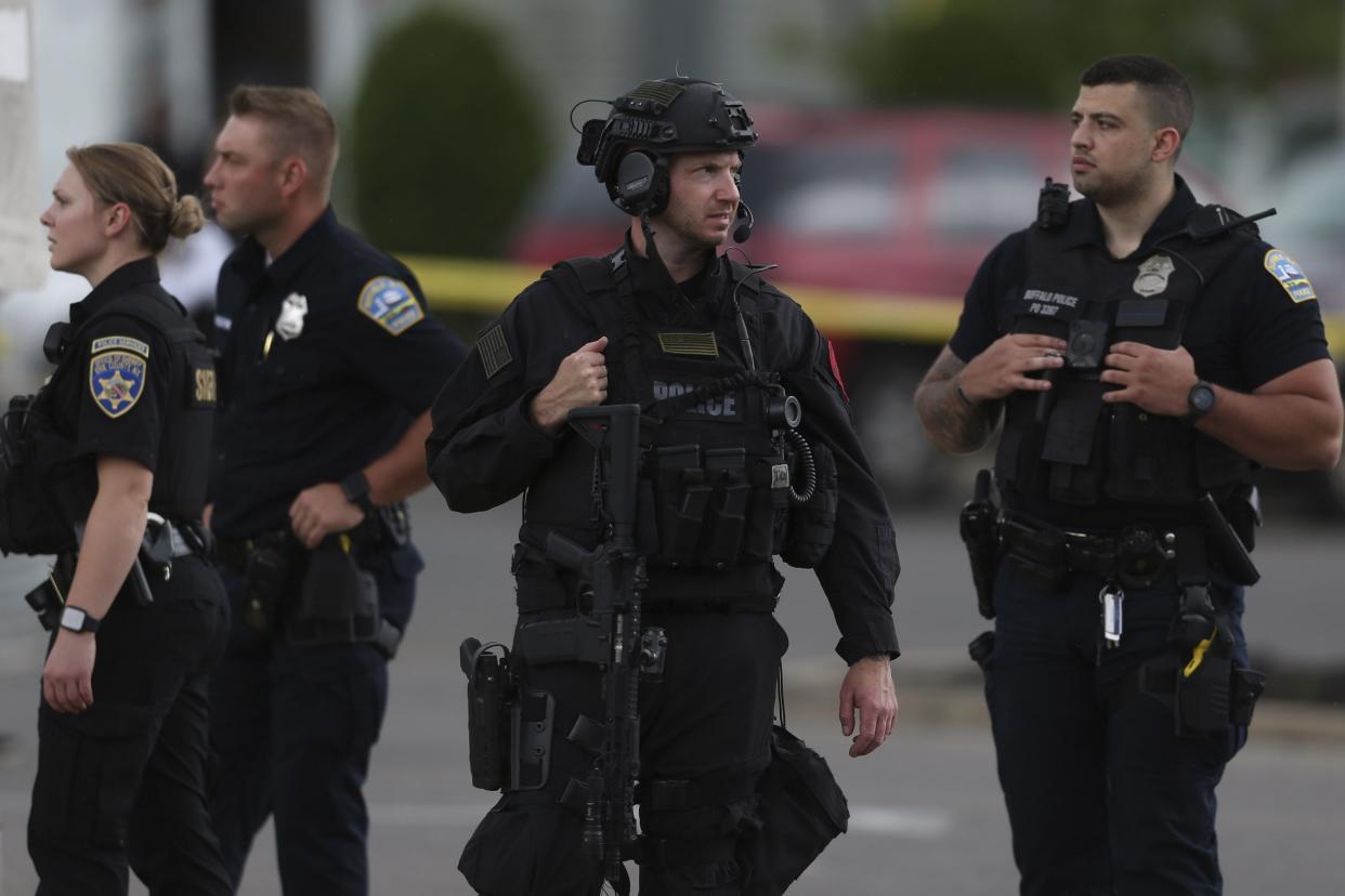 Police walk along the perimeter of the scene after a shooting at a supermarket on Saturday, May 14, 2022, in Buffalo, N.Y.  Officials said the gunman entered the supermarket with a rifle and opened fire. Investigators believe the man may have been livestreaming the shooting and were looking into whether he had posted a manifesto online.