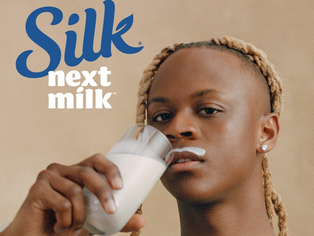 Myles O'Neal holds a glass of Silk Nextmilk while sporting a milk mustache in an ad for the brand. The copy reads "nextmilk is a better milk."