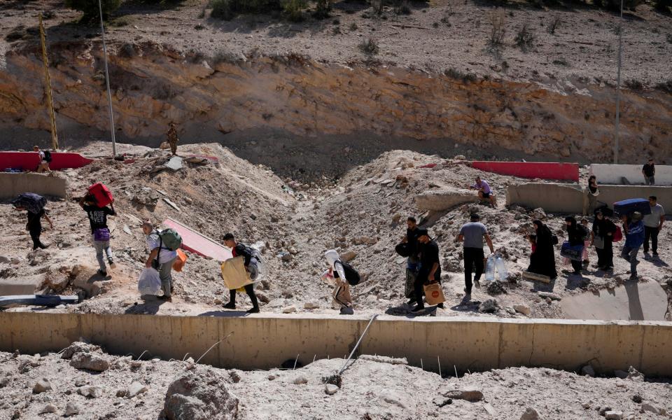 People carry their luggage as they cross into Syria on foot