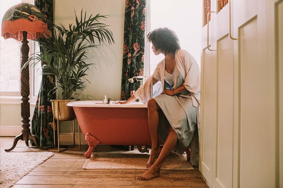 woman perching on the side of a roll top bathtub in a luxurious room online Interior design services