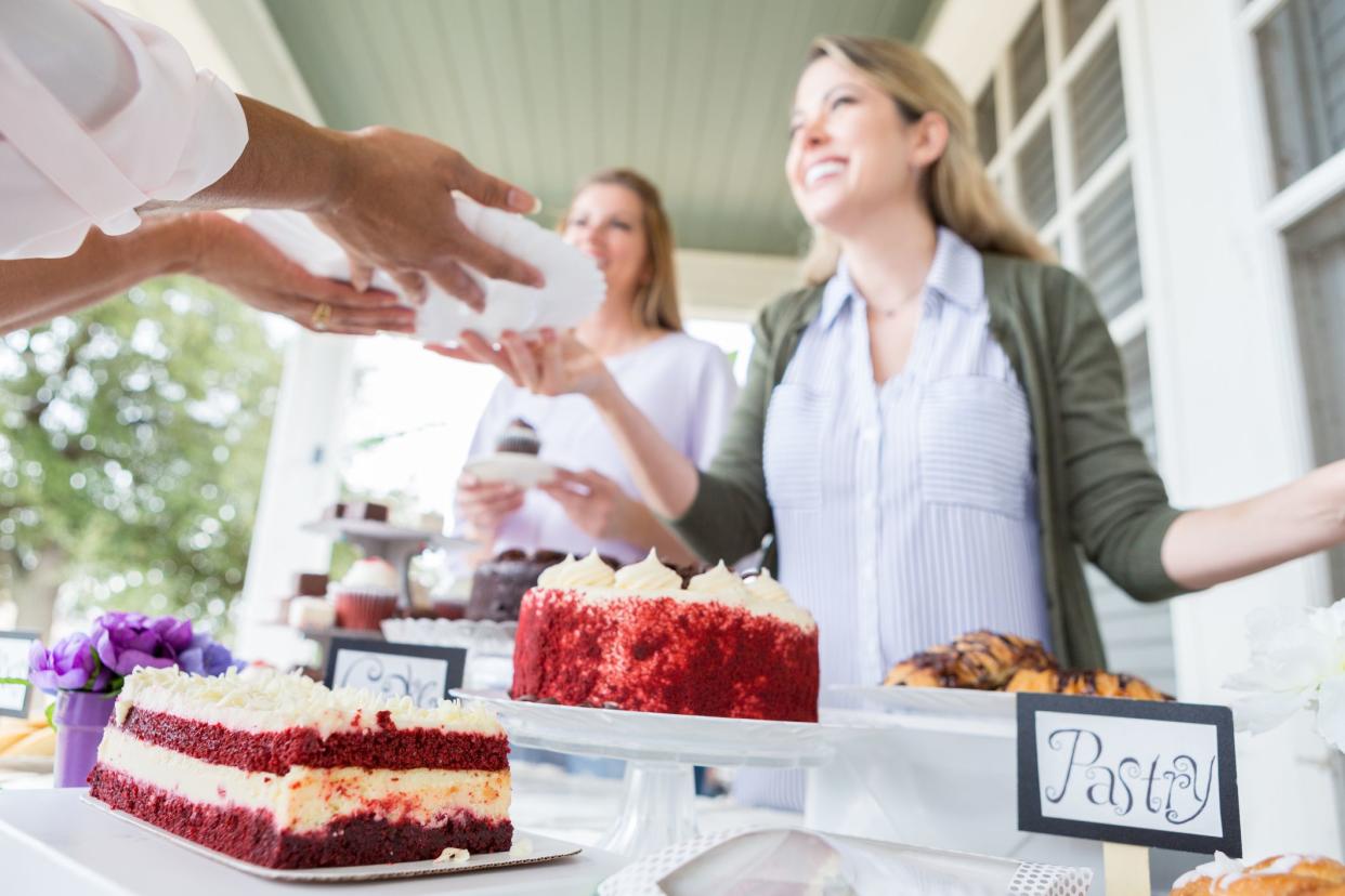 Cheerful women enjoy selling baked goods at a charity event to raise funds for cancer research. They are serving a customer.