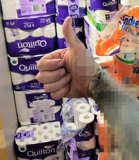 A man pictured with several packets of toilet paper and hand towels.