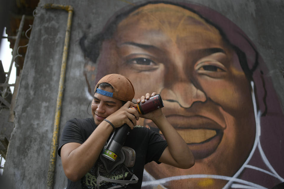 Street artist Wolfgang Salazar mixes spray paint backdropped by his most recent art mural featuring Venezuelan athlete Yulimar Rojas, in the Boleita neighborhood of Caracas, Venezuela, Saturday, Jan. 2, 2021. Salazar uses the artistic name of Badsura, a play on the English word “bad” and the Spanish word “basura," for “garbage,” (AP Photo/Matias Delacroix)