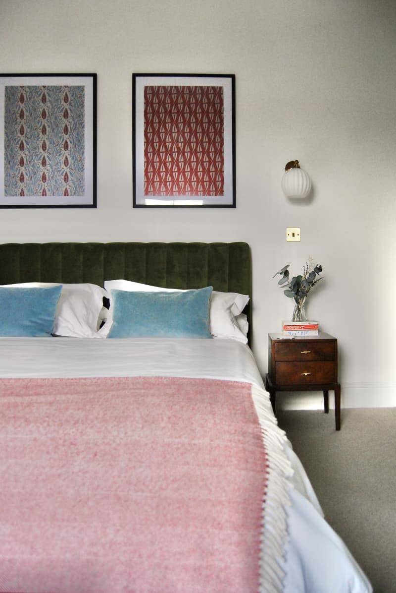 Bed with a blue pillow, green headboard, and framed art above.