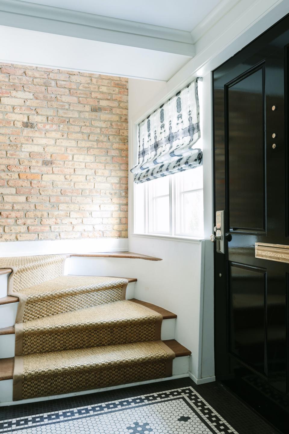 Entryway with neutral stairs above a bare brick wall and open door.