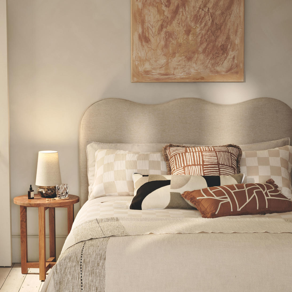  Cream bedroom with abstract art on wall, wavy head board and natural coloured bedding. 