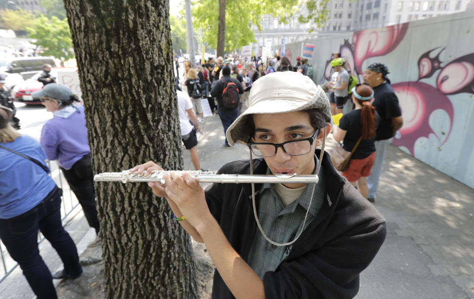 Mikaele Baker plays the flute as he stands on the side of the street of anti-fascist groups counter-protesting as members of Patriot Prayer and other groups supporting gun rights demonstrate across the street during a rally, Saturday, Aug. 18, 2018, at City Hall in Seattle. (AP Photo/Ted S. Warren)