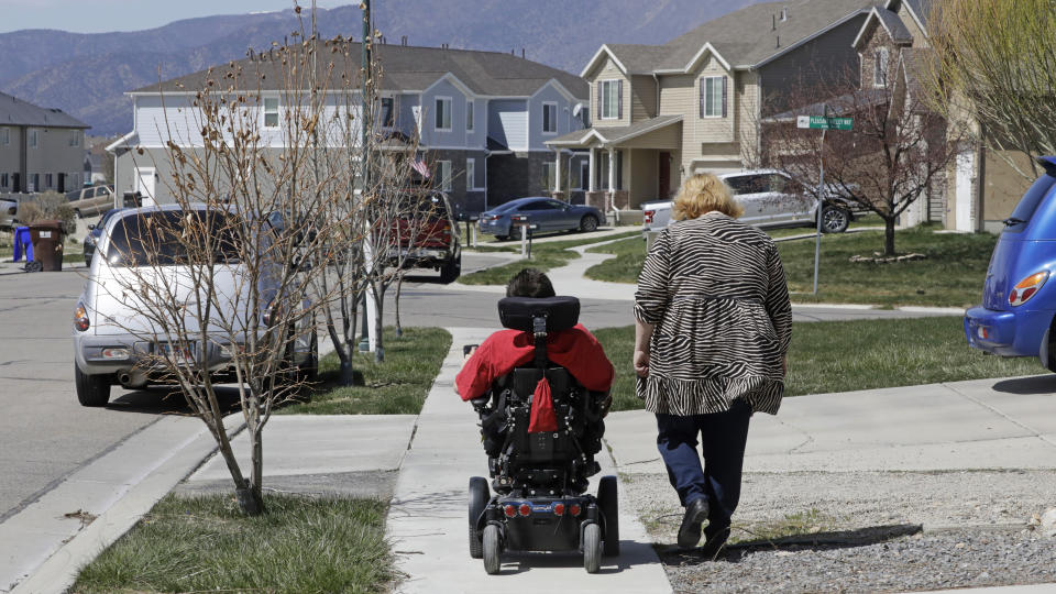 In this April 14, 2020, photo, Jodi Hansen walks with her son Jacob Hansen near their home in Eagle Mountain, Utah. Even before the new coronavirus hit, cystic fibrosis meant a cold could put Jacob Hansen in the hospital for weeks. He relies on hand sanitizer and disinfecting wipes to keep germs at bay because has cerebral palsy and uses a wheelchair, but these days shelves are often bare. For millions of disabled people and their families, the coronavirus crisis has piled on new difficulties and ramped up those that already existed. (AP Photo/Rick Bowmer)
