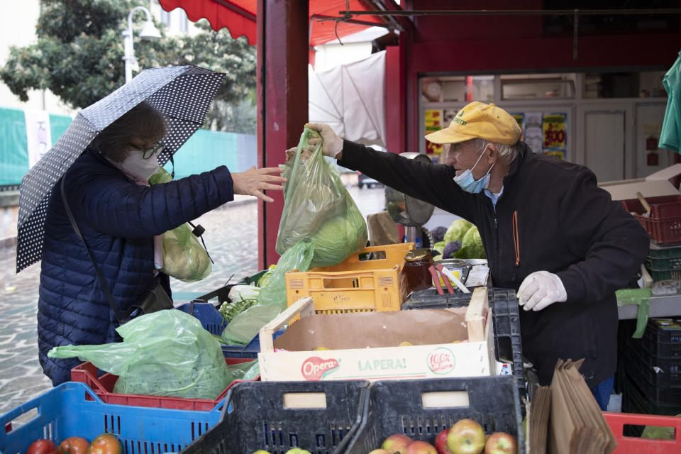 Domenico Zoccoli, 80, serves a client in the open air market where he works, in Rome, Wednesday, Dec. 2, 2020. In Italy, which has the world's second-oldest population, many people in their 70s and older have kept working through the COVID-19 pandemic. From neighborhood newsstand dealers to farmers bring crops to market, they are defying stereotypic labels that depict the old as a monolithic category that's fragile and in need of protection. (AP Photo/Alessandra Tarantino)