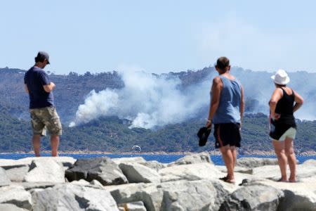 Tourists look smoke that rises from trees at a forest fire on La Croix-Valmer from Cavalaire-sur-Mer, near Saint-Tropez, France. REUTERS/Jean-Paul Pelissier