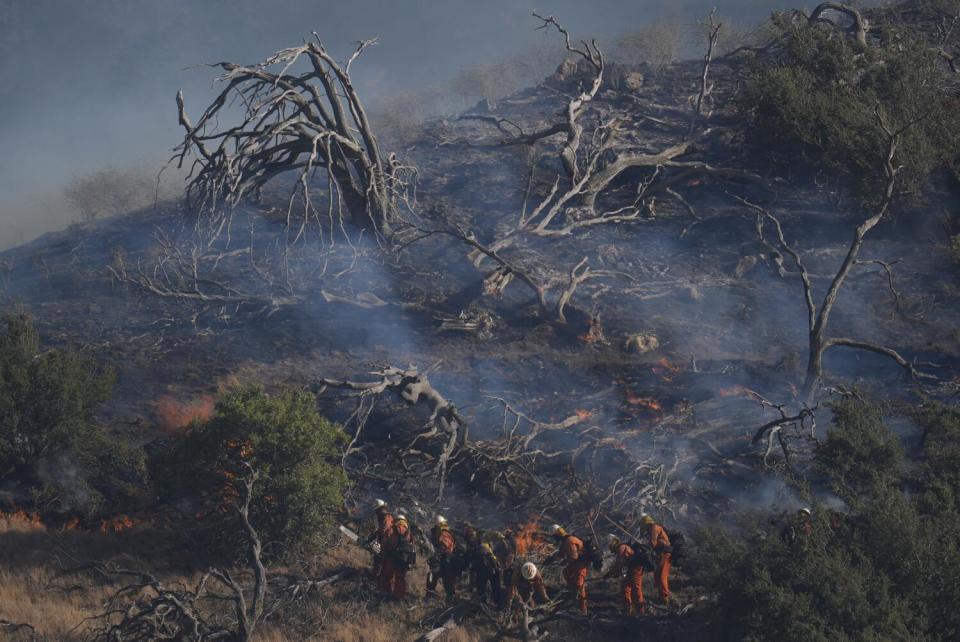 Firefighters work under a smoldering hillside left behind by the Post Fire