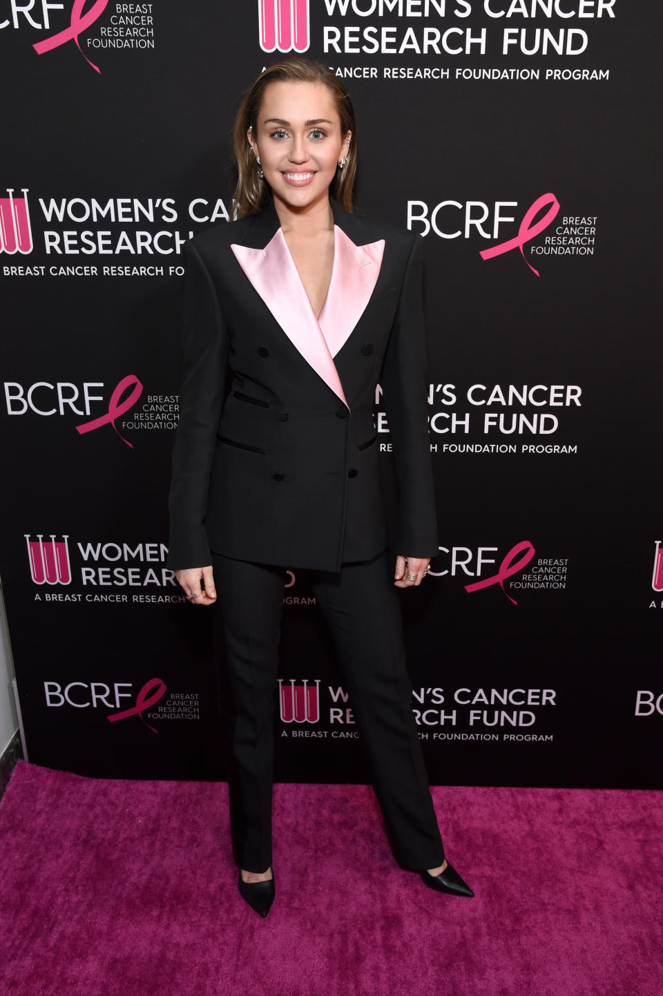 Miley Cyrus attends WCRF's "An Unforgettable Evening" at the Beverly Wilshire Four Seasons Hotel on February 28, 2019 in Beverly Hills, California. She wears a black fitted suit with baby pink lapels, a double breasted blazer and pointy-toed high heels.