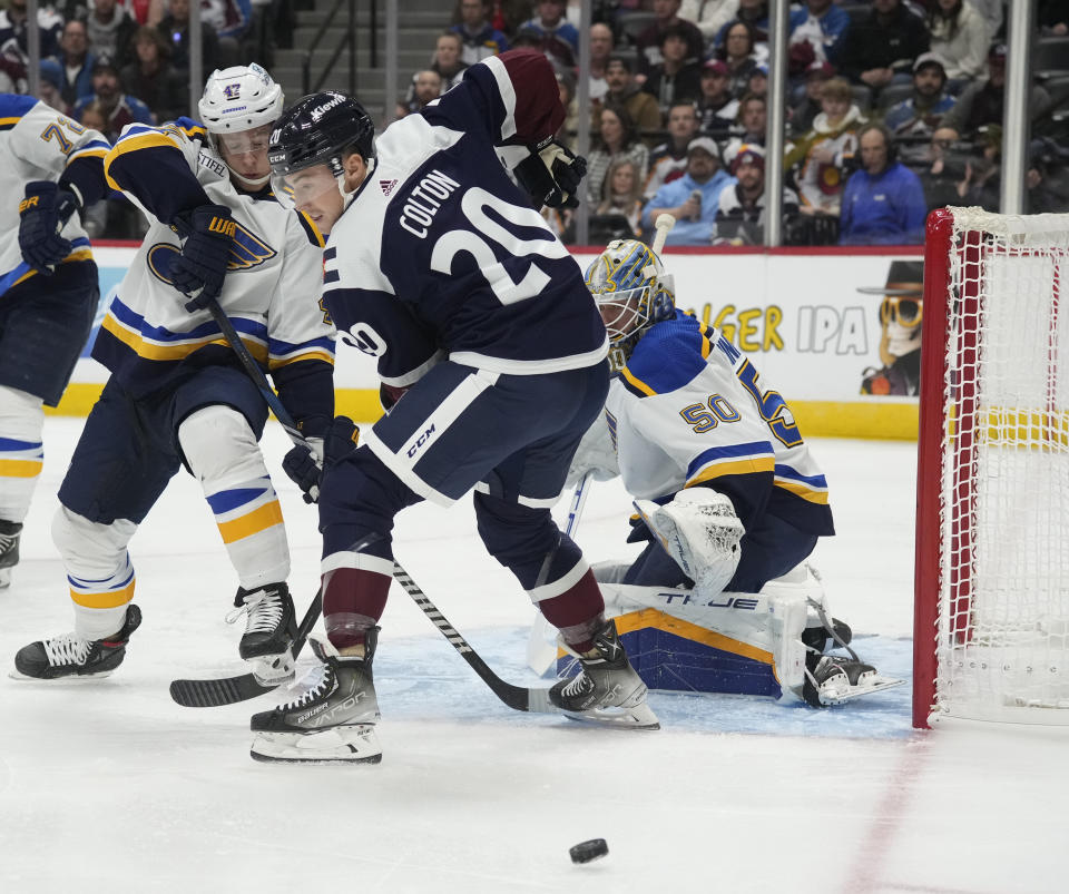 St. Louis Blues defenseman Torey Krug, left, knocks the puck away from Colorado Avalanche center Ross Colton as Blues goaltender Jordan Binnington watches during the first period of an NHL hockey game Saturday, Nov. 11, 2023, in Denver. (AP Photo/David Zalubowski)