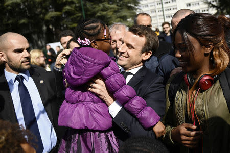 French presidential election candidate for the En Marche ! movement Emmanuel Macron (C) holds a young girl as he greets people during a campaign visit to Sarcelles, near Paris, on April 27, 2017. REUTERS/Martin Bureau