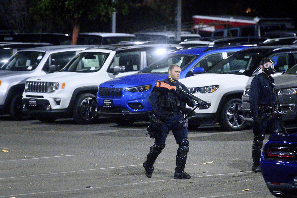 FILE - In this Monday, June 1, 2020, file photo, a police officer searches a San Leandro, Calif., car dealership shortly after multiple vehicles were stolen. Police say many of the smash-and-grab thefts have been carried out by caravans of well-coordinated criminals that have coincided with or followed protests over the death of George Floyd, who was killed by a Minneapolis police officer who pressed his knee into Floyd's neck. Nearly 75 vehicles were stolen Sunday, including models driven through glass showroom doors to escape. (AP Photo/Noah Berger, File)